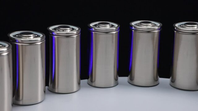 Closeup of manufacture of new high-capacity lithium batteries on a production line with flashing blue backlight on the black background
