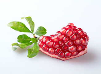 A piece of pomegranate with scattered grains and pomegranate leaves, isolated on a white background