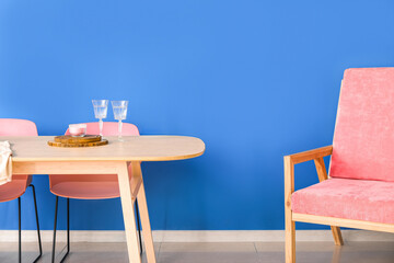 Comfy armchair and wooden table near color wall
