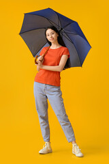 Beautiful teenage girl with open blue umbrella on yellow background