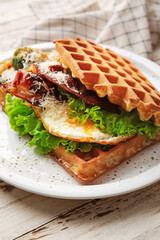 Delicious Belgian waffles with egg, bacon and vegetables in plate on light wooden background, closeup