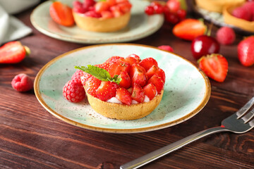 Plate with tasty berry tart on wooden background