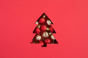 Christmas tree cut out on the red  background and filled with colored balls. Copy space. Close-up.
