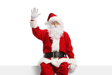 Cheerful santa claus sitting on a panel and waving - obrazy, fototapety, plakaty