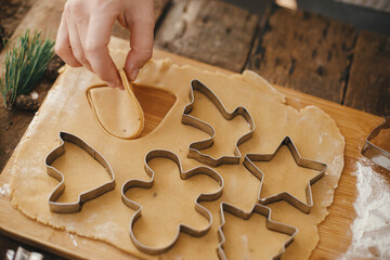 Making traditional christmas gingerbread cookies on rustic table with spices and decorations. Hand cutting gingerbread dough with christmas metal cutters on wooden board, moody image