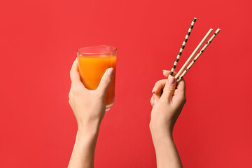 Female hands with glass of healthy juice and straws on color background
