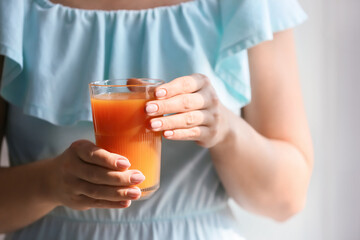 Woman with glass of healthy juice in room, closeup