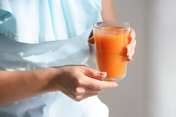 Woman with glass of healthy juice in room, closeup