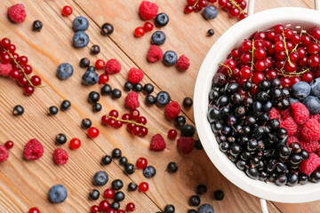 Colander with different ripe berries on wooden background, closeup