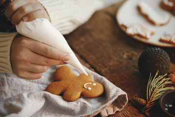 Hands decorating christmas gingerbread man cookie with frosting on rustic table with napkin,...