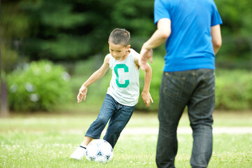緑の芝生の上で元気よくサッカーをして遊ぶ男の子と父親