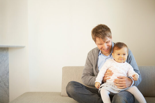 ソファーの上で笑顔の赤ちゃんを抱いて笑う父親