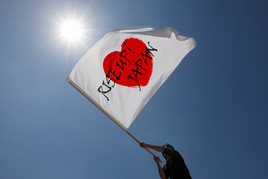 青空と太陽の下でRISE UP! JAPANと書かれた旗を振る男性