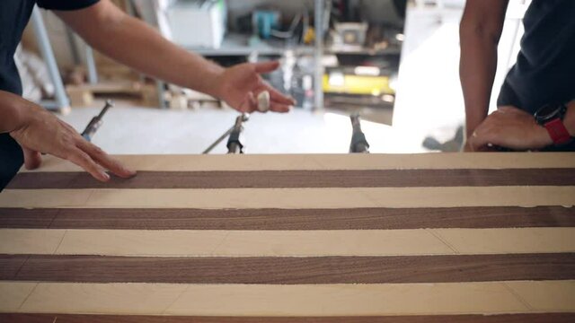 Craftsmen working in workshop with wood materials, carpenter using steel clamps for tightening glued wooden bars on workbench. Artisan joiners using carpentry tools for creating wood masterpiece