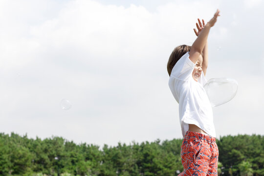 青空の下でシャボン玉をよけるハーフの男の子