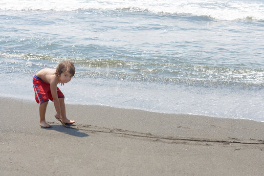 波打ち際で砂浜に絵を描いて遊ぶ水着姿のハーフの男の子