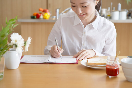 朝手帳にスケジュールを書く女性と朝ごはん