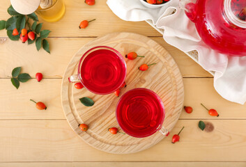 Glass cups of tasty rose hip tea and berries on wooden background