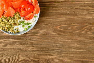Bowl with tasty rice, salmon, tomato and pumpkin seeds on wooden background