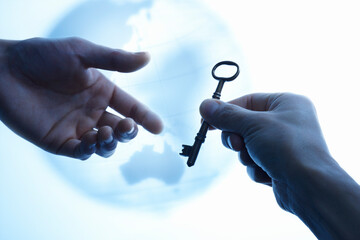 地球儀を背景にアンティークな鍵を渡そうとしている2本の手
