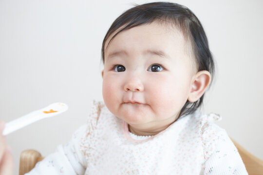 お母さんにスプーンで離乳食を食べさせてもらう笑顔の赤ちゃん