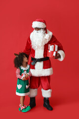 Cute little elf with Santa Claus and gifts on red background