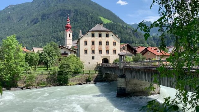 The cold stream and the traditional church and wooden bridge of Pfunds in Austria