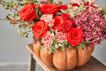 Flowers arrangement in pumpkin on wooden table. Fresh cut flowers for decoration home. European floral shop. Delivery fresh cut flower.