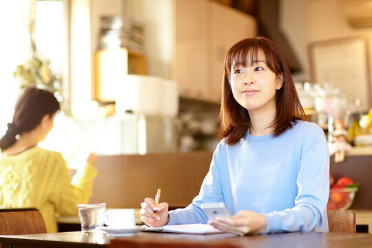 カフェで携帯電話を見ながらスケジュール帳を確認する女性
