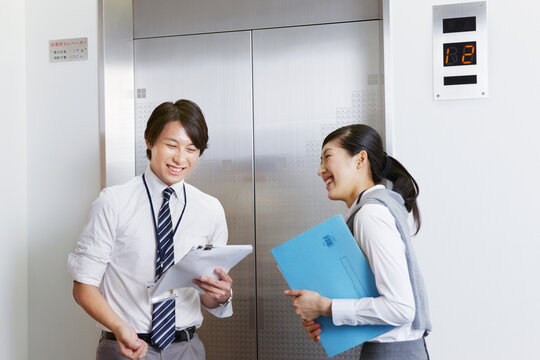 エレベーター前で会話するスーツの女性とビジネスマン