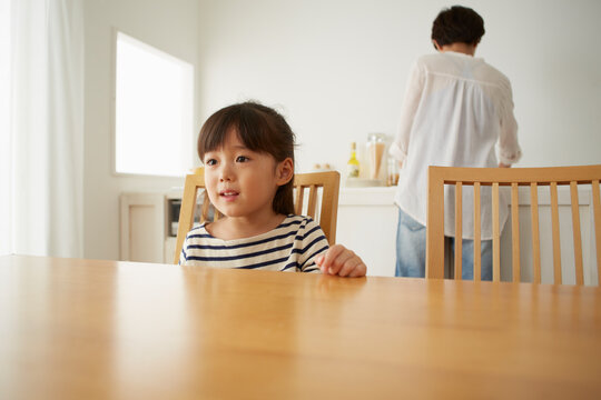 キッチンで料理をする母親とテーブルで待つ女の子