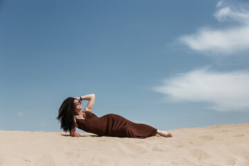 Dark brunette with voluminous curly hair among the Sands in a sand dune in a flying dress