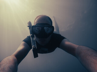 Male free diver taking a selfie while diving into the blue.