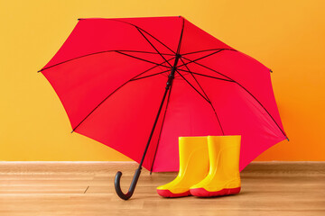 Pair of rubber boots with umbrella near color wall