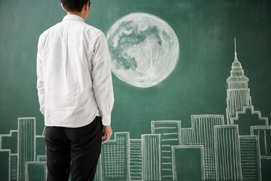 ビル群と満月が描かれた黒板イラストの前に立つ人