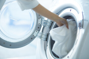 ドラム式洗濯機に洗濯物を入れる女性の手
