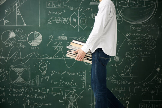 黒板の前でたくさんの本を持つ