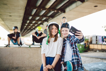 Two teenage girls taking a selfie photo on a smartphone in a skate park. Friendship concept. Children create social media content over the phone while posing for the camera on a skate park ramp