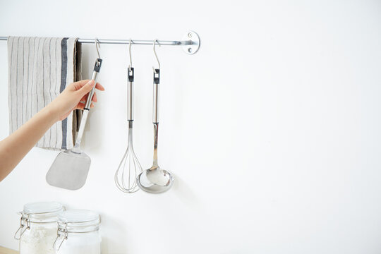 バーに下がったキッチンツールを取る女性の手
