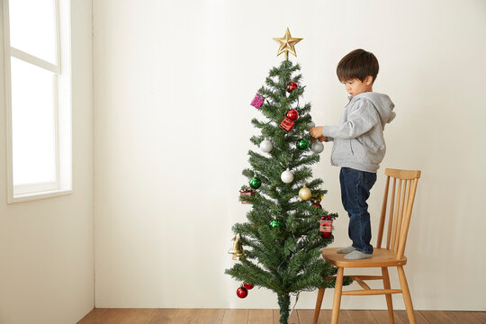 椅子を台にしてクリスマスツリーの飾り付けをする男の子