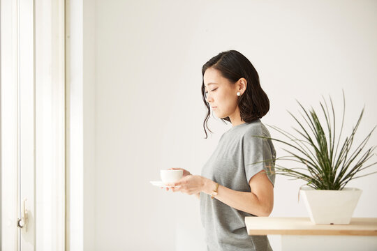 窓辺にたたずみコーヒーを飲む女性