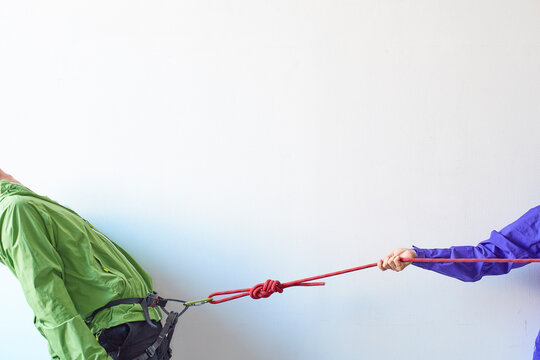 白い壁の前でカラビナがかかったハーネスを引っ張られる登山者