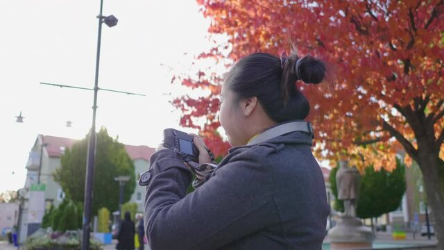 Asian woman standing and taking a picture by camera outside. Beautiful red and green trees background, wearing winter outfits in beautiful day on the holiday, Sweden