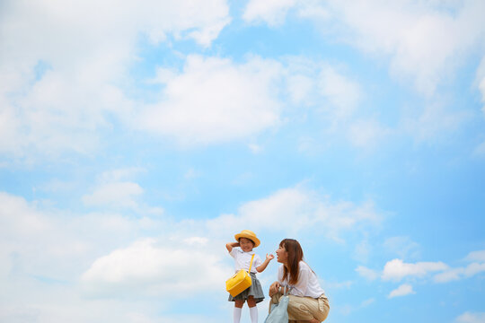 青空を背景に幼稚園児の女の子に話しかけるお母さん