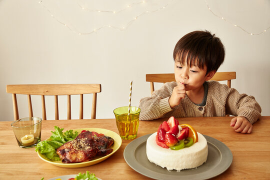 パーティーの準備がされているテーブルでケーキのクリームをなめる男の子