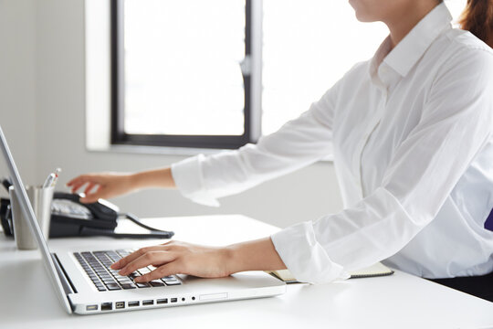 オフィスでノートパソコンをしながら受話器に手をかける女性