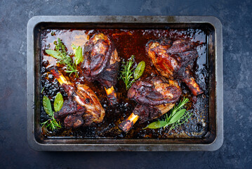 Traditional braised slow cooked lamb shank in red wine sauce with herbs served as top view in a barbecue metal sheet