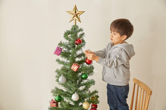 椅子を台にしてクリスマスツリーの飾り付けをする男の子