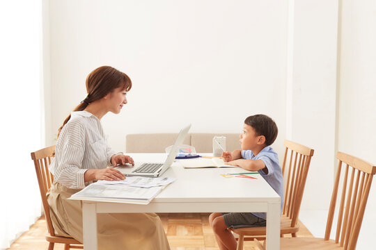 ダイニングテーブルで在宅ワークをする女性と勉強する男の子