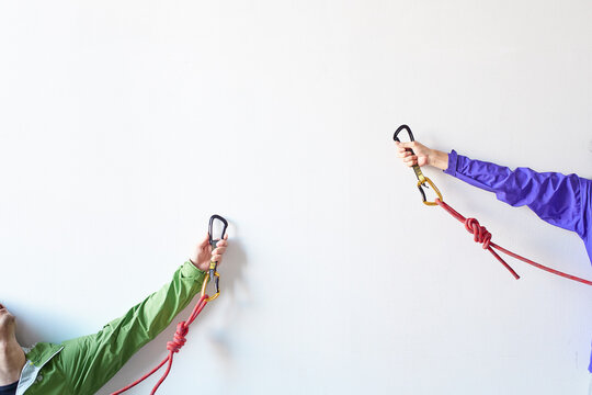 白い壁の前でロープを持ち体を伸ばしてカラビナを引っ掛けようとする２人の登山者